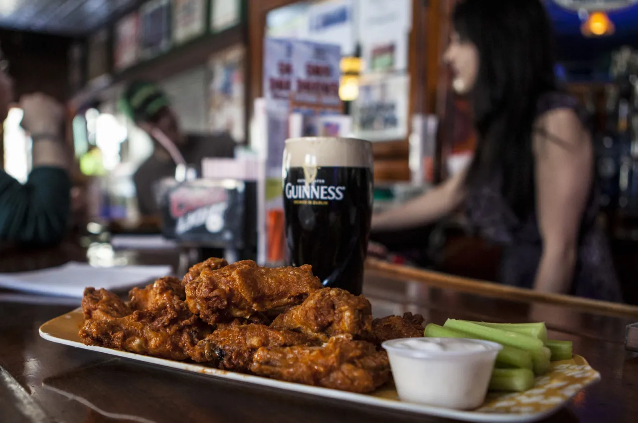 a plate of wings sits on a bar next to a full pint of Guiness.