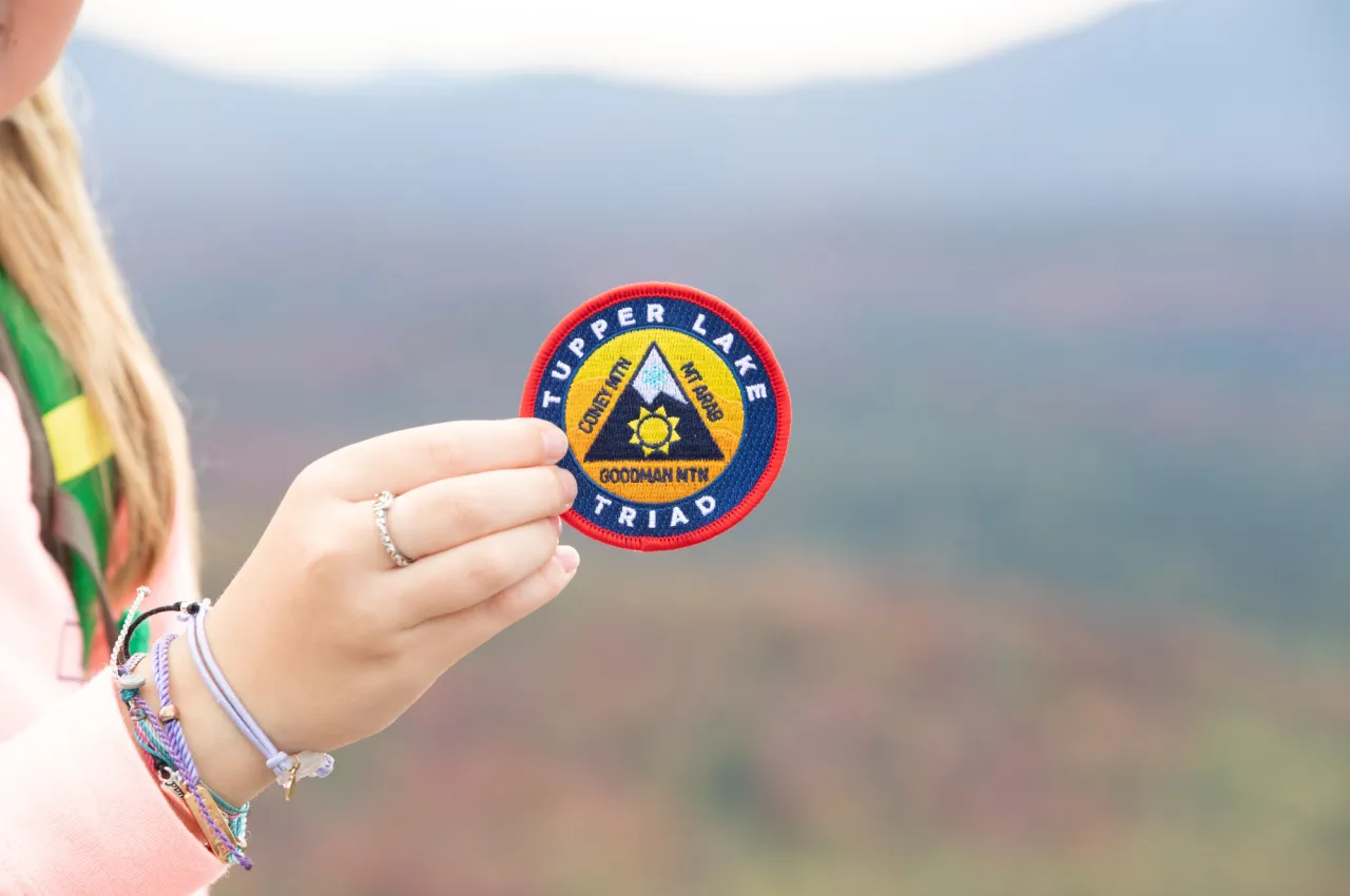A young person's hand holds the Tupper Lake Triad patch