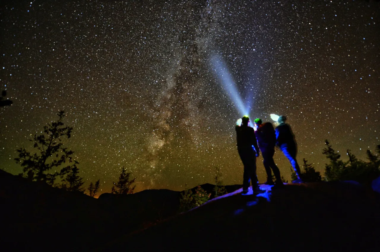 Three people shine headlamps into the night sky where the milky way is visible
