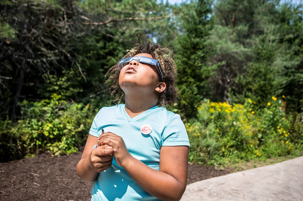 A girl looking up at the sky with eclipse glasses on