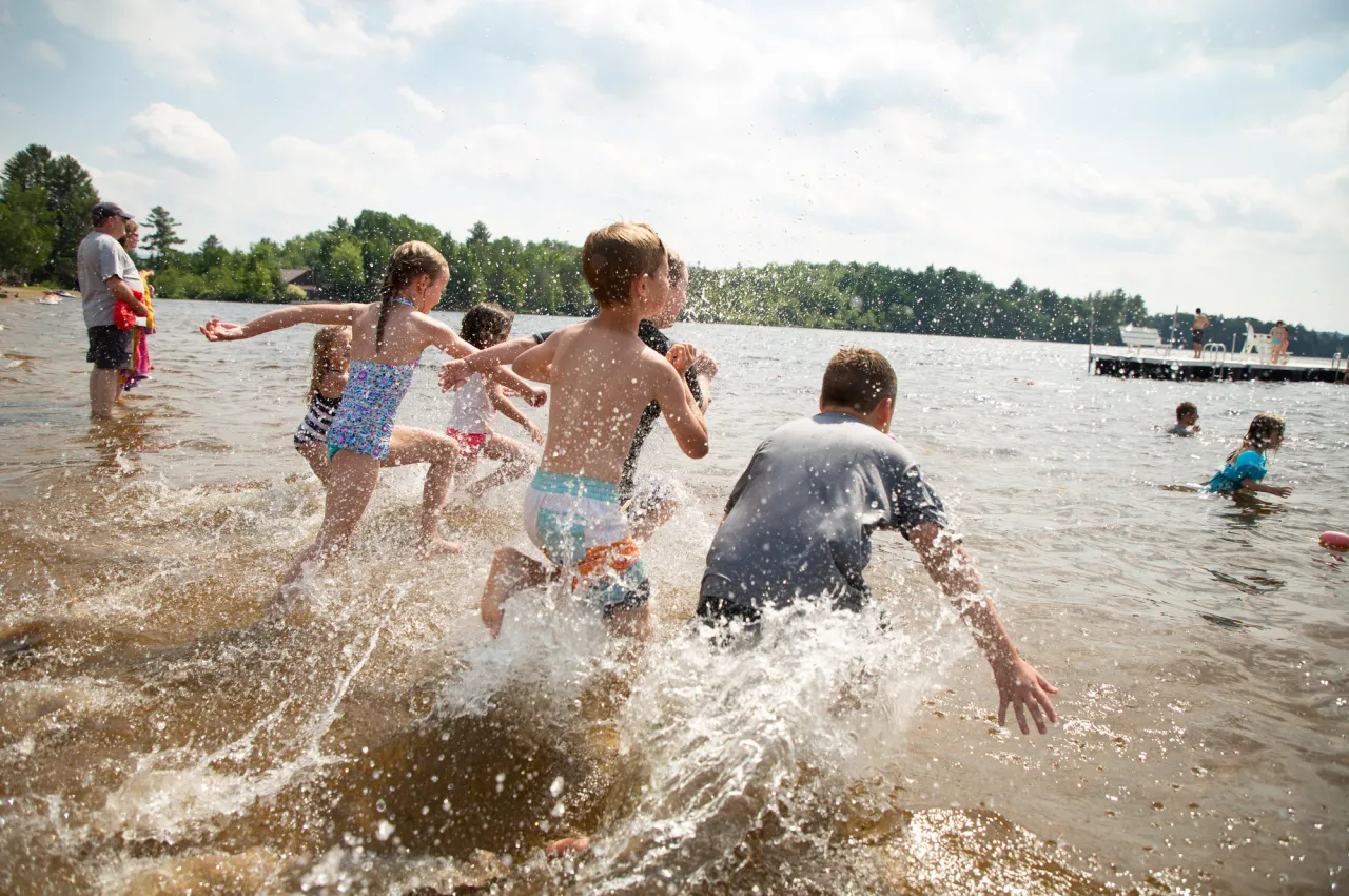 A group of children run splashing into a lake on a sunny summer day.