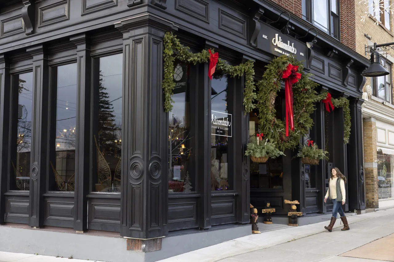 A woman walking into a sleek store front with a giant green wreath and greenery hung out front.