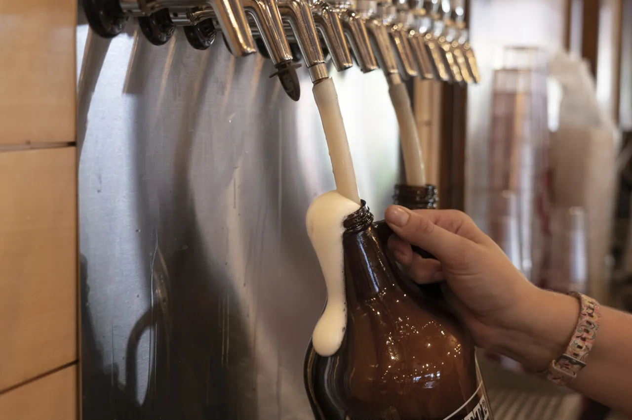 A person fills up a growler of beer from the tap. 