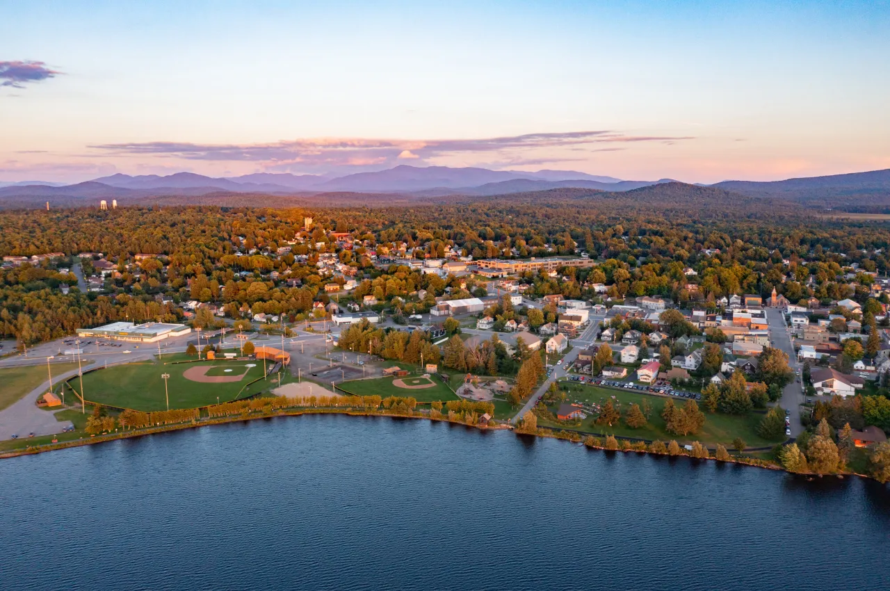 An aerial view of the village of Tupper Lake during sunset, illuminating the mountains in the background.