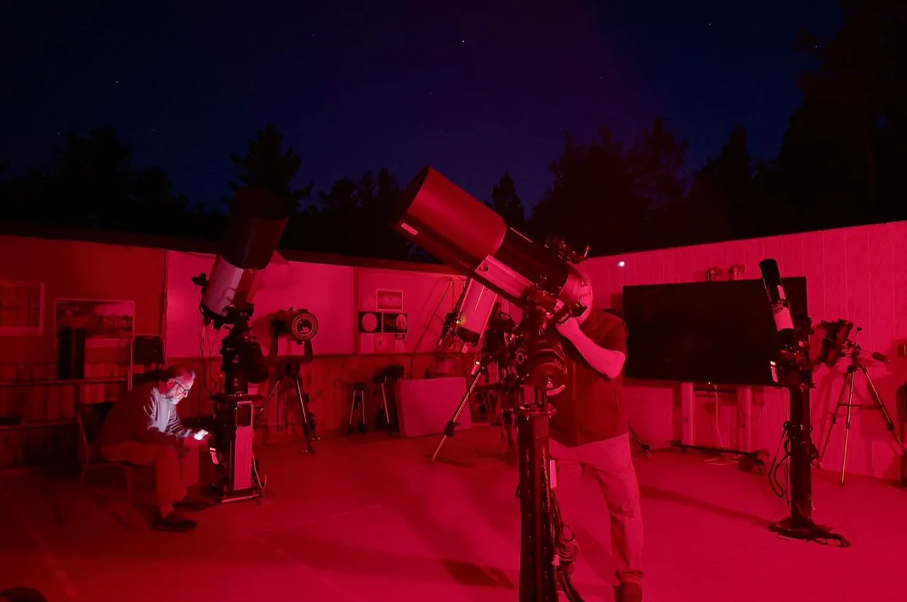 Stargazers utilize telescopes in red light at an open-roof observatory