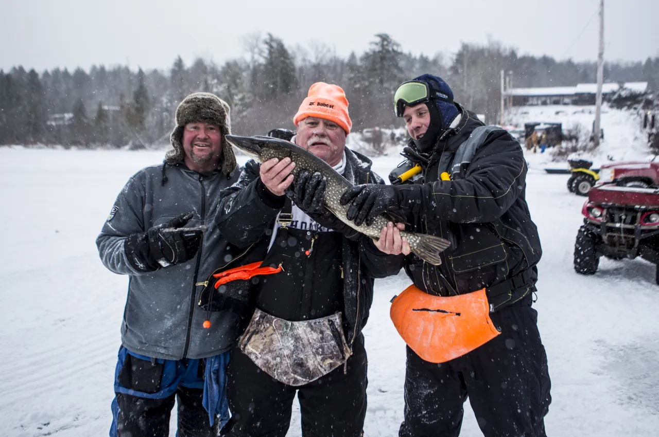 3 men hold their catch of the day on the ice of Simond Pond. 