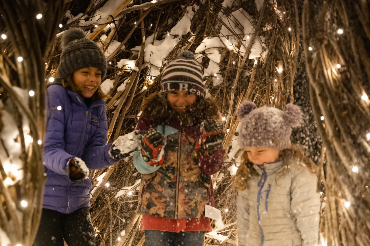 3 girls throw snow and laugh during Wild Lights.