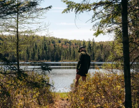 A hiker stands at the edge of an opening to a pond