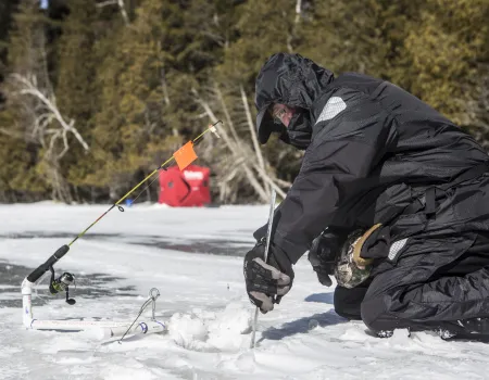 An ice fisher cutting a hold in the ice