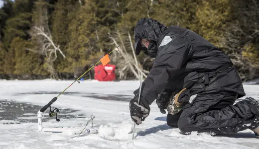 An ice fisher cutting a hold in the ice