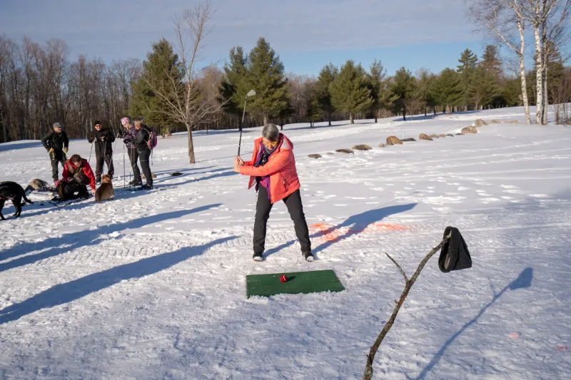 A golfer tees off in the snow.