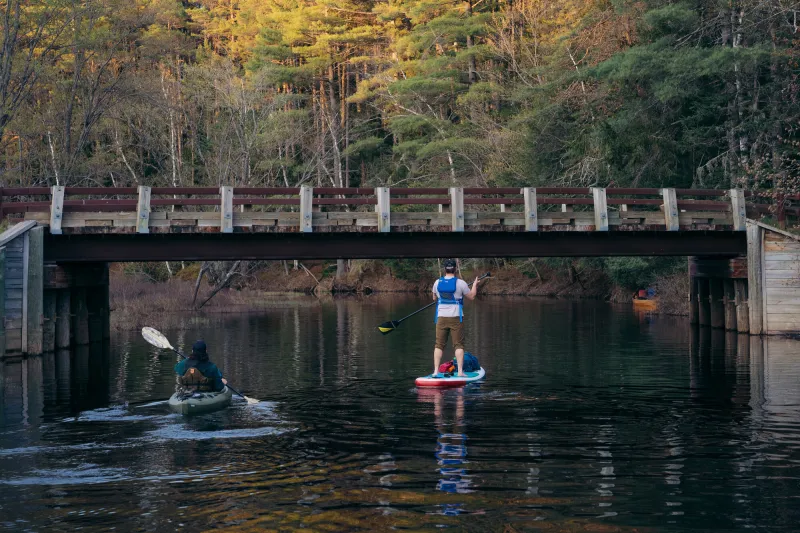 A kayaker and paddleboarder about to go under a bridge