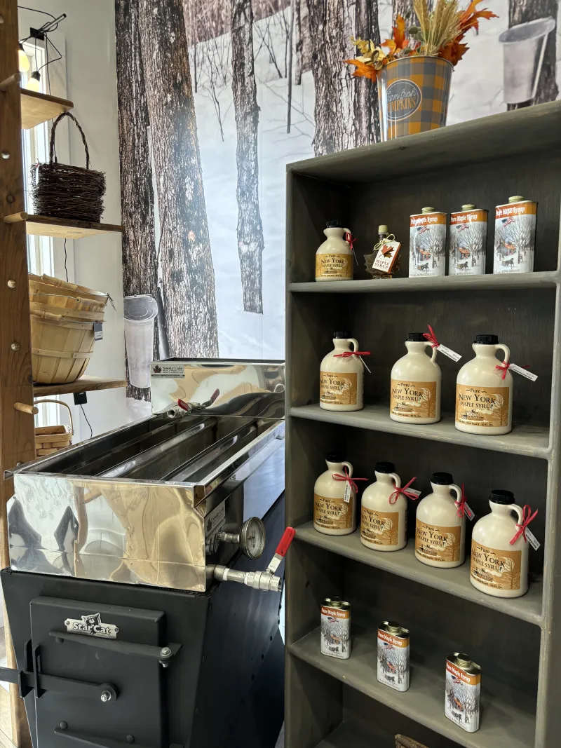 A store display of maple syrup on shelves next to a vintage sap boiler.