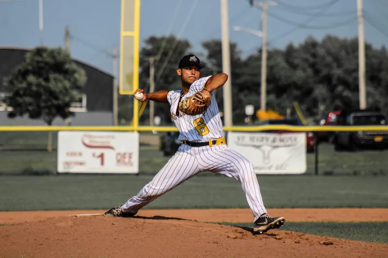 A baseball player pitches from a mound on a sunny day.