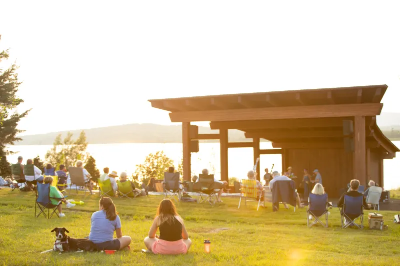 A bandshell at sunset surrounded by flowers and people listening to music.