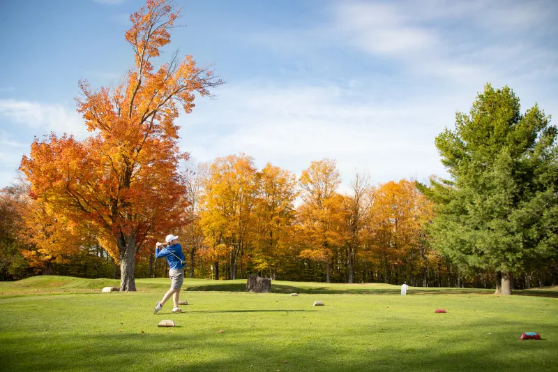 A guy golfs surrounded by fall foliage