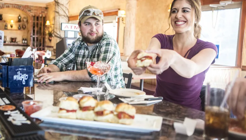 A woman holds a chicken parm slider at a bar