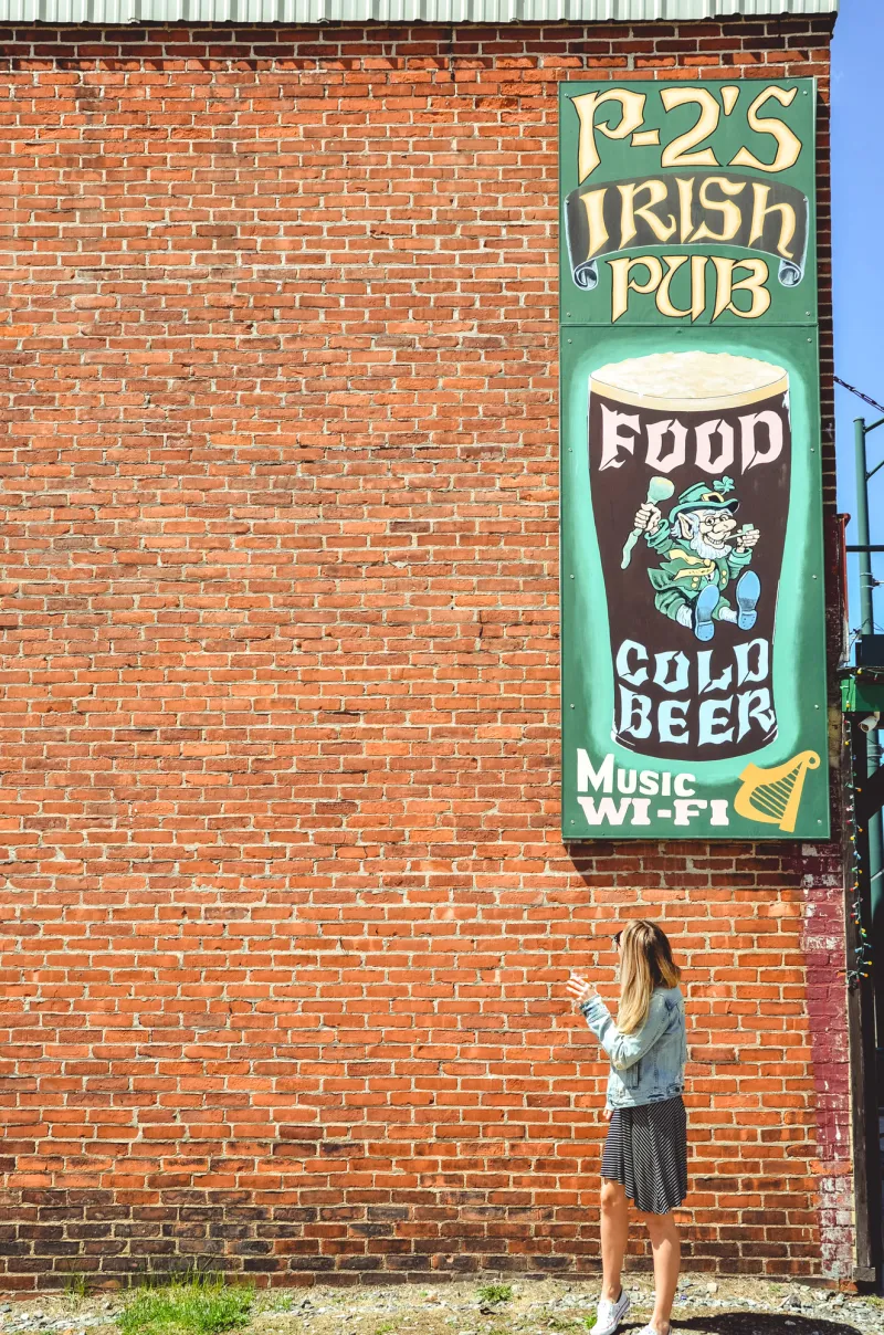 A woman looks up at an Irish pub sign on a brick building.