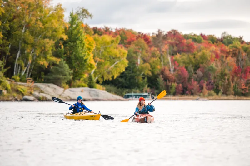 Two women paddle a lake in fall.