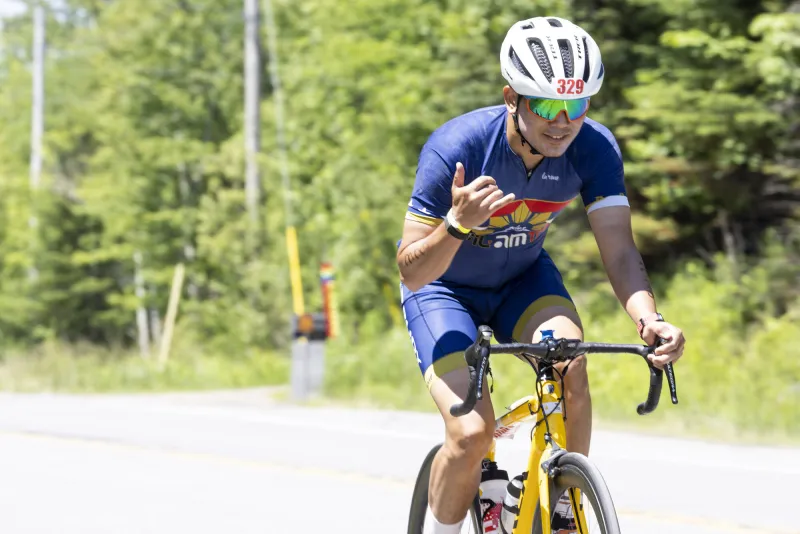 A male cyclist flashes a pinky and thumb salute while cycling.