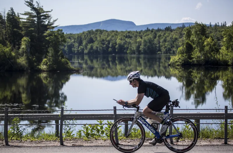A cyclist rides past a lake and mountain views while competing in a triathlon.