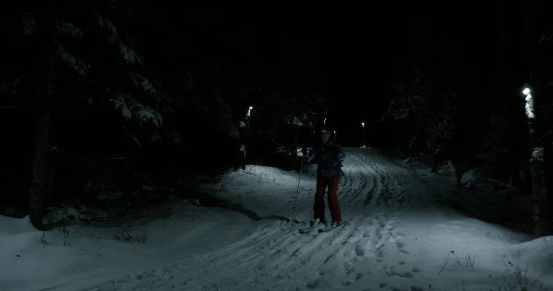 A lone cross-country skier glides down a lit trail at night.