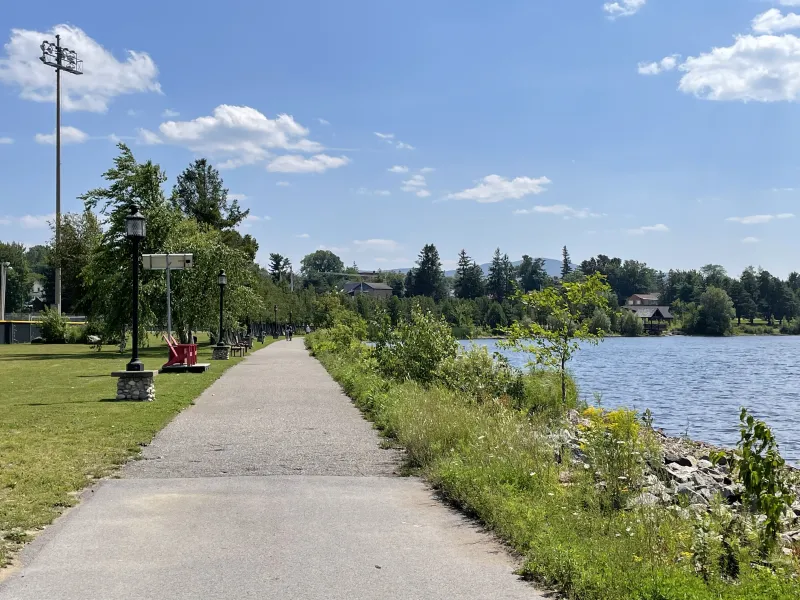 Looking along the paved trail with a pond on the right and trees on the left.