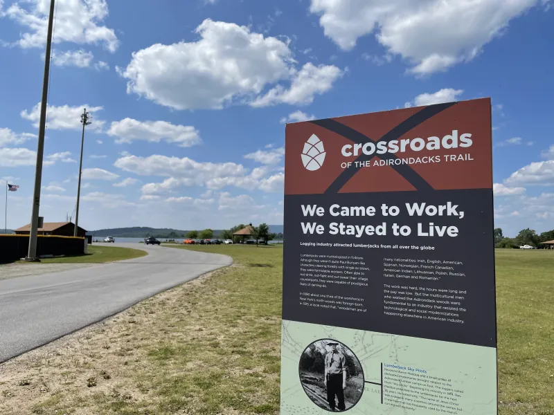 A sign shares information about local history with blue skies and a large flatwater pond in the background.