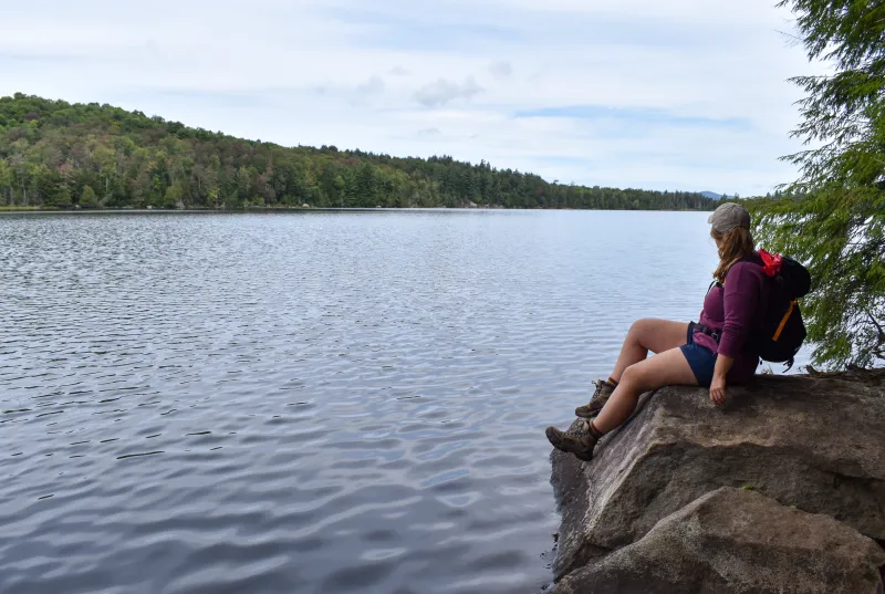 A woman sits on a rock on the shore of a pond.