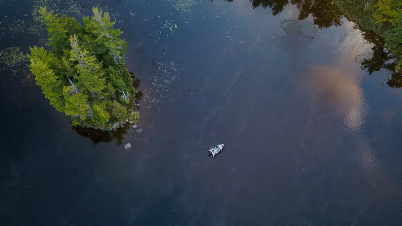 Aerial view above a fishing boat on a blue lake with a nearby island with pine trees