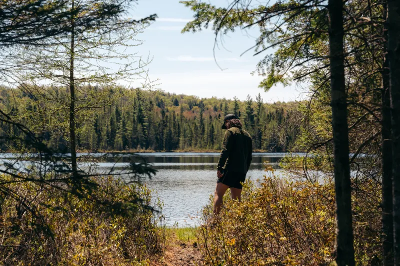 A man stands besides a small pond in the trees