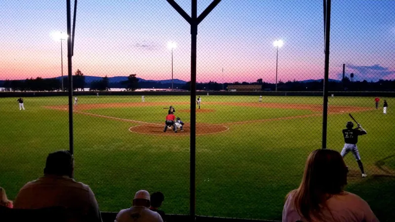 In the middle of an inning of baseball with the sun setting behind the outfield. Someone is at bat.