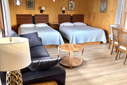 The interior of a motel room with hardwood floor, double beds and pine walls.