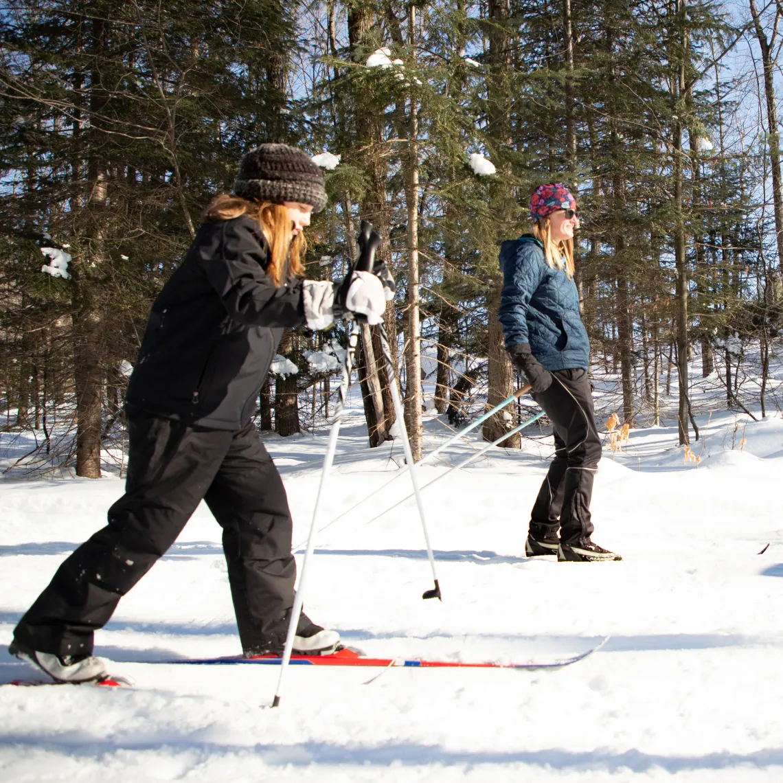 A woman and daughter cross country ski on a groomed trail.