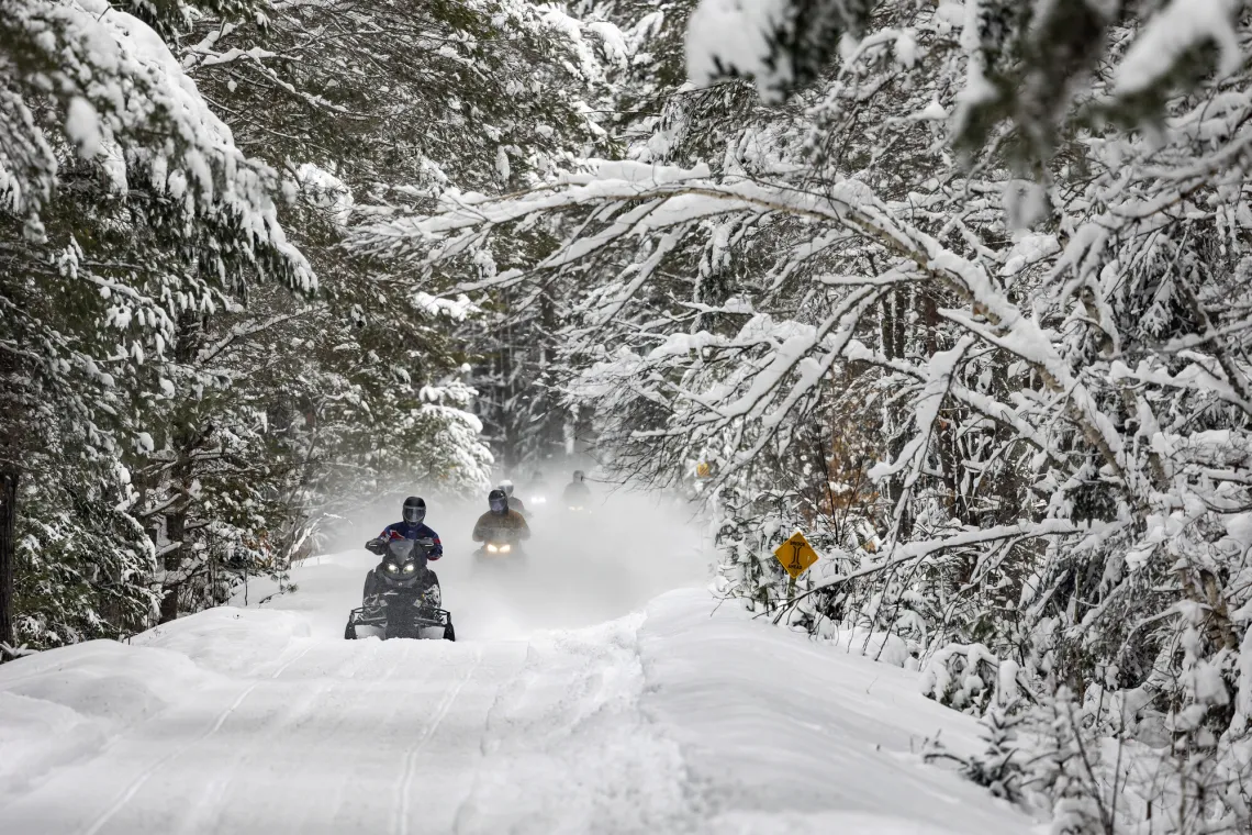 Snowmobiles zoom down the wide groomed trail.