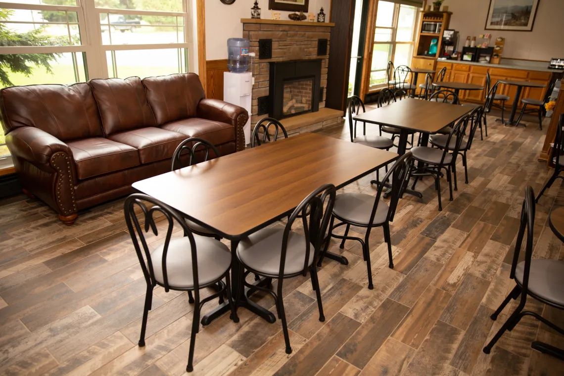 The breakfast area of a motel, featuring wooden tables surrounded by chairs in front of large windows.