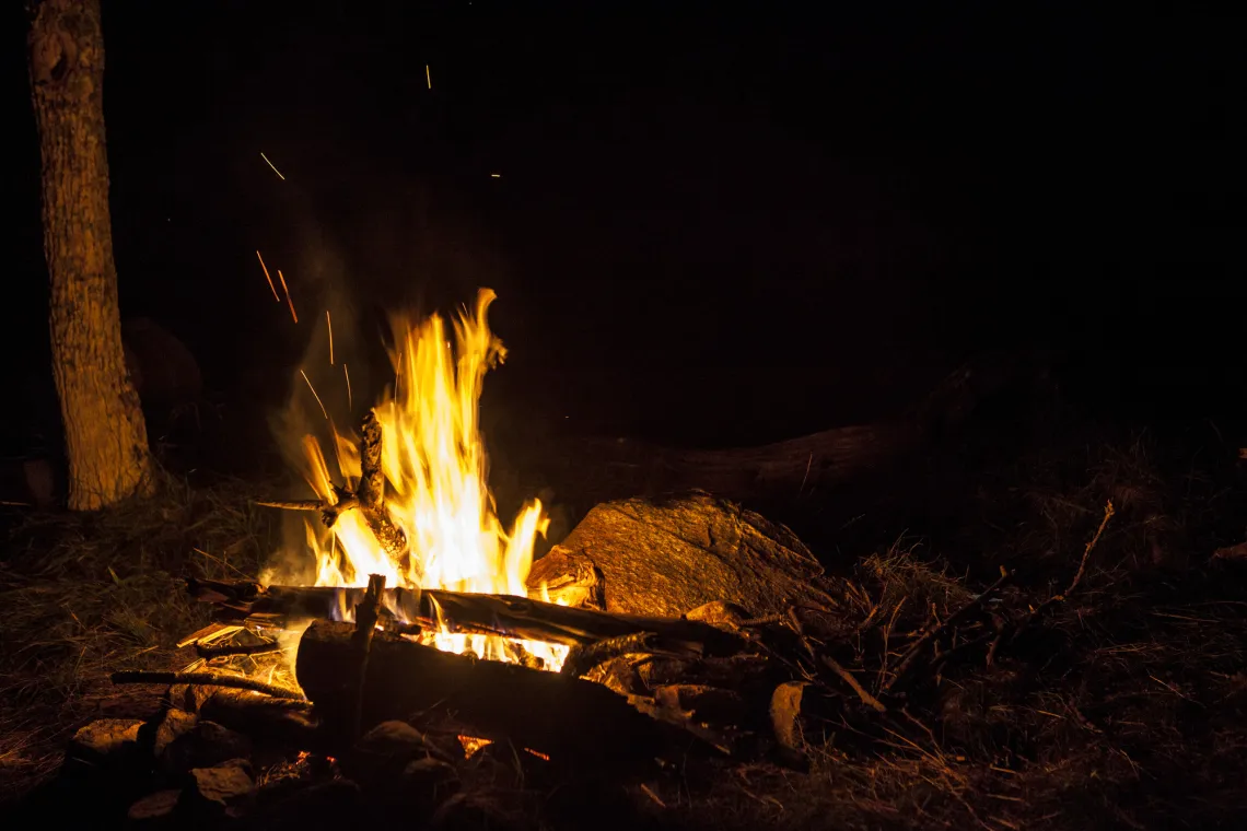 A fire pit bordered by an assortment of rocks lights up in the darkness in Tupper Lake