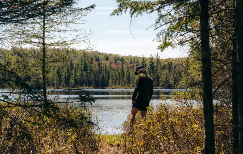 A hiker stands at the edge of an opening to a pond