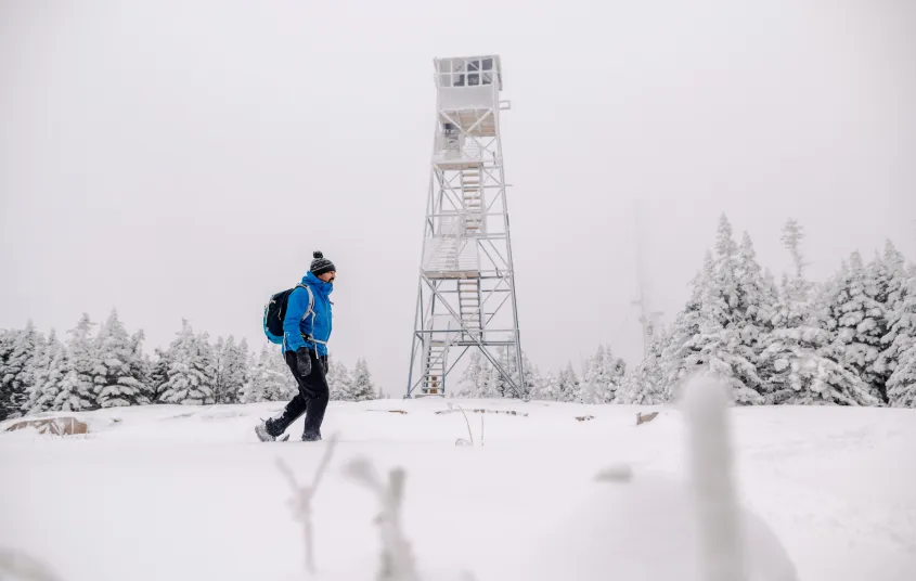 A man walks in front of a firetower in the winter