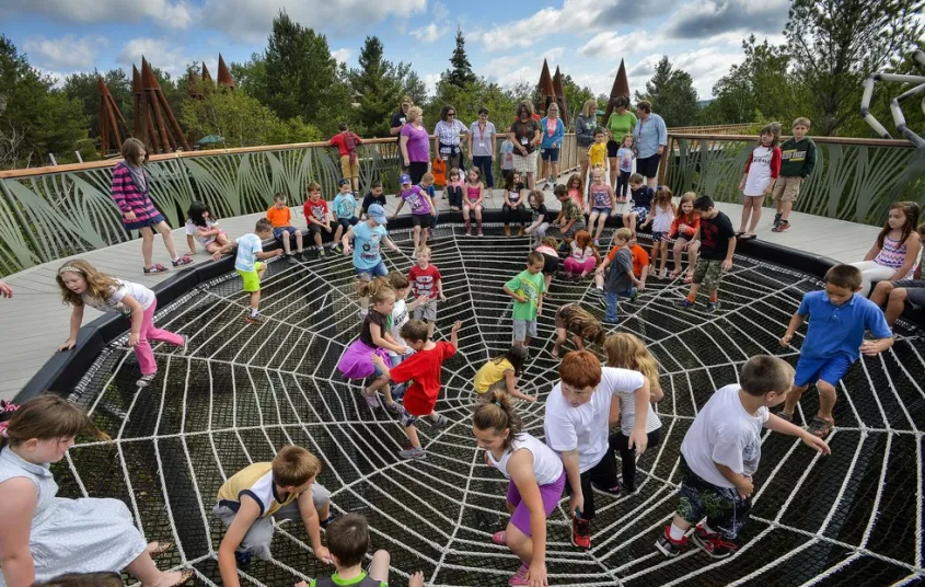 Dozens of children playing on the outdoor spiderweb exhibit