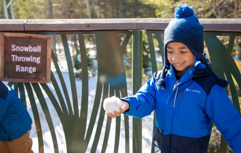 A young child gleefully looks down at his hand holding a freshly made snowball