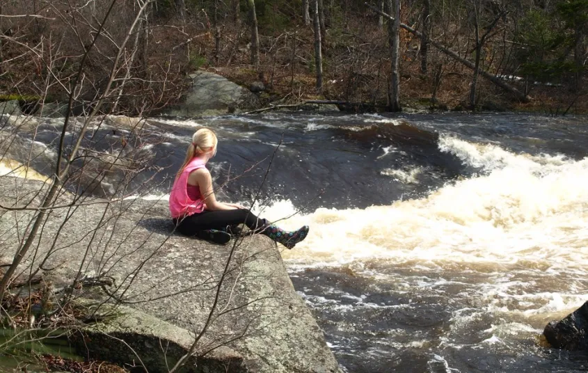 A woman sits next to a waterfall