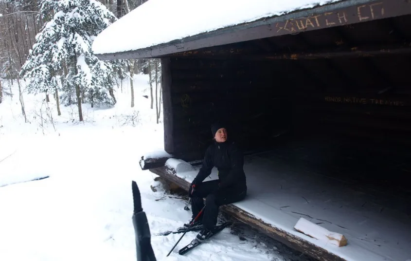 A person sits in a lean-to in the winter