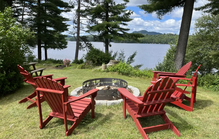 Adirondack Chairs circling a fire pit overlooking the lake through the trees