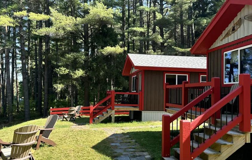 Side view of cabins with porches&#44; adirondack chairs surrounding fire pits and large pine tree boarder