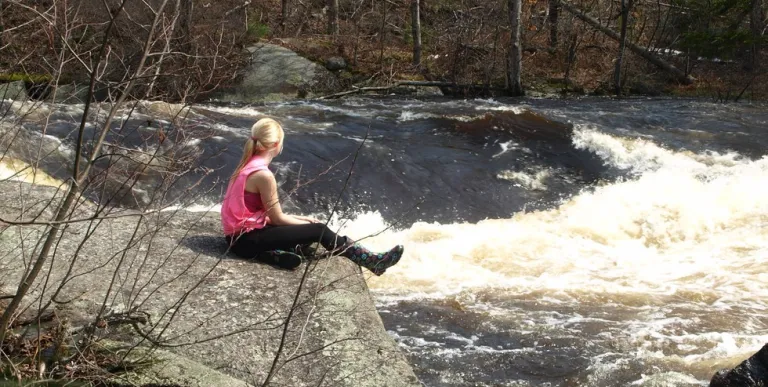 A woman sits next to a waterfall