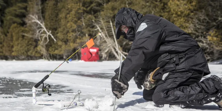 An ice fisher cutting a hold in the ice
