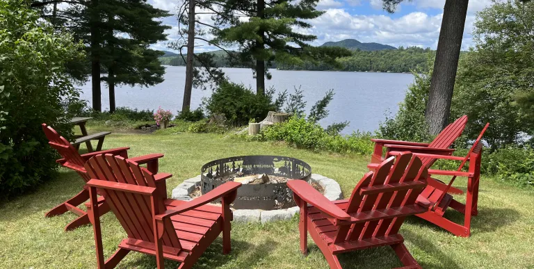 Adirondack Chairs circling a fire pit overlooking the lake through the trees